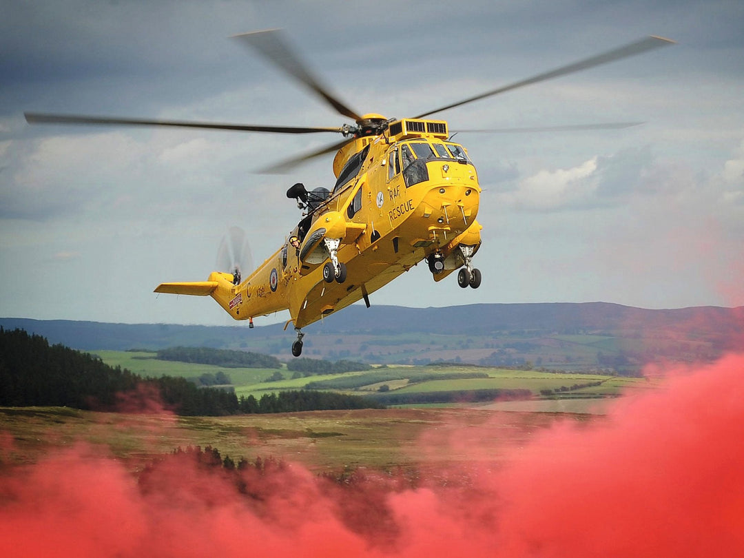 A yellow RAF Search and Rescue Sea King trains over the hills with red smoke billowing beneath it, September 2011