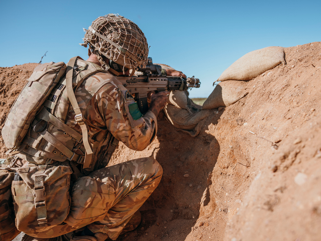 A british Army Soldier firing a rifle from a trench